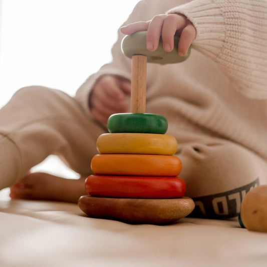Child playing with a stack of colorful QToys wooden rings on a light surface.