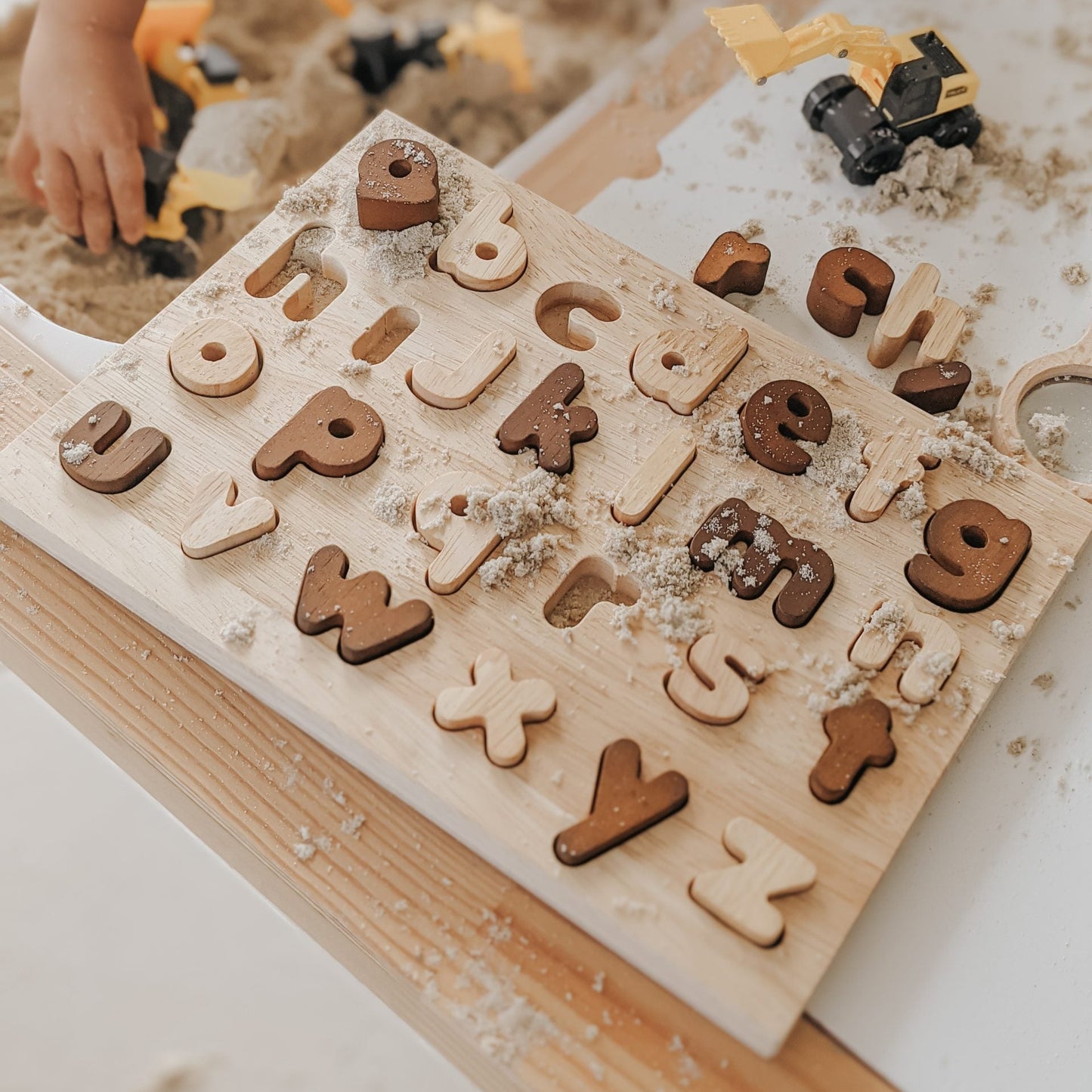 Wooden alphabet puzzle with children playing with toy trucks in the background